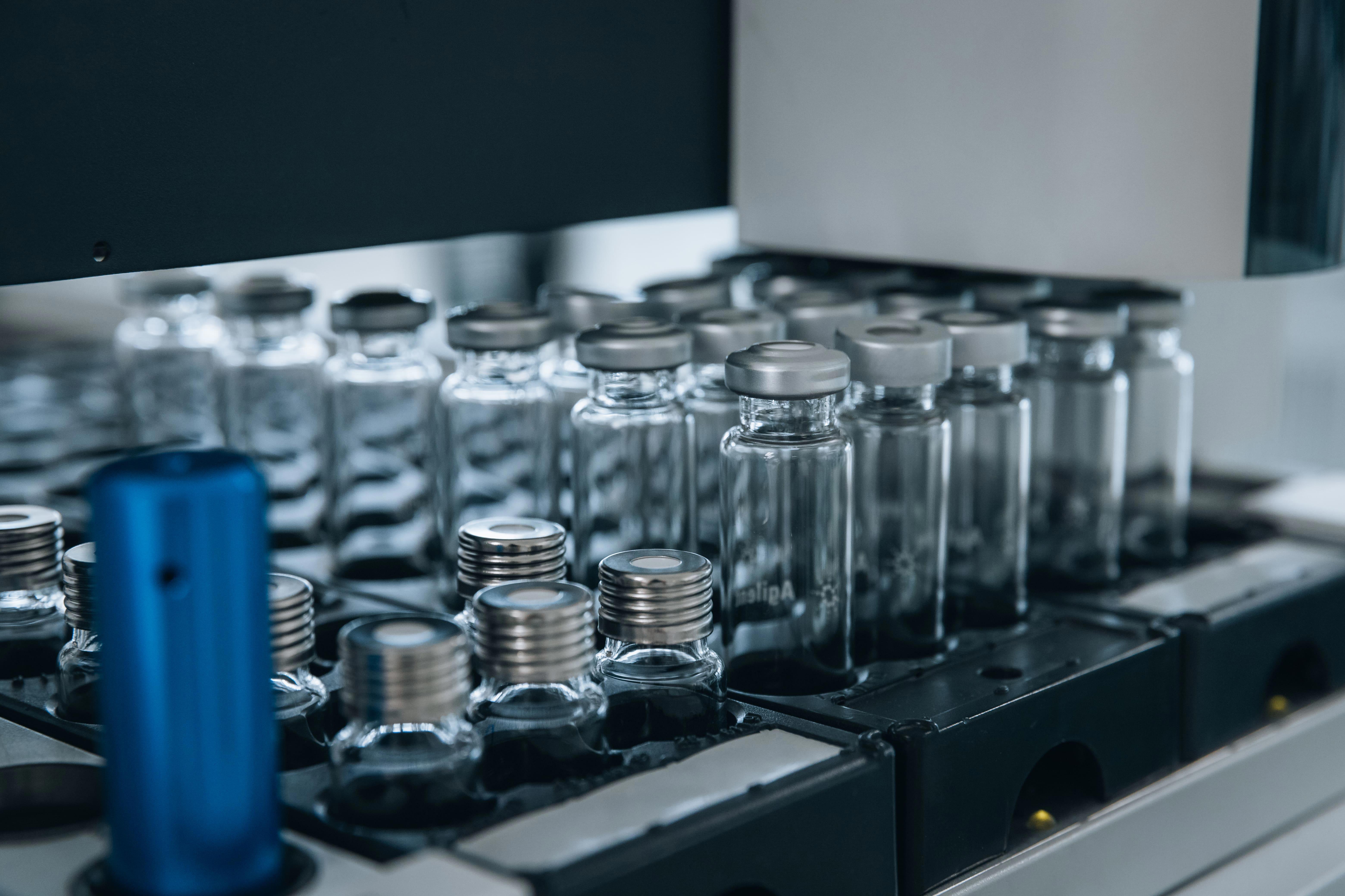 Gros plan sur des fioles en verre transparent, fermées par des capsules métalliques argentées, disposées en rang sur un équipement de laboratoire automatisé. L’image illustre les procédures de collecte et d’analyse des résidus de stérilisation menées par Eurofins BioPharma Product Testing dans un environnement pharmaceutique contrôlé.