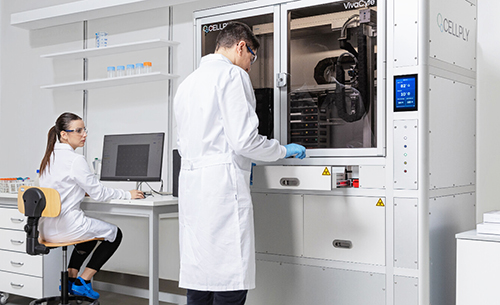 Laboratoire Eurofins équipé de technologies avancées, avec deux techniciens en blouses blanches. L’un travaille sur un ordinateur, l’autre utilise un appareil automatisé de culture ou d’analyse cellulaire marqué "Q.CELLY" et "VivoCyt". L’environnement comprend des étagères organisées avec flacons et contenants, illustrant un espace de recherche moderne dédié aux analyses cellulaires, au développement pharmaceutique et aux services CDMO.