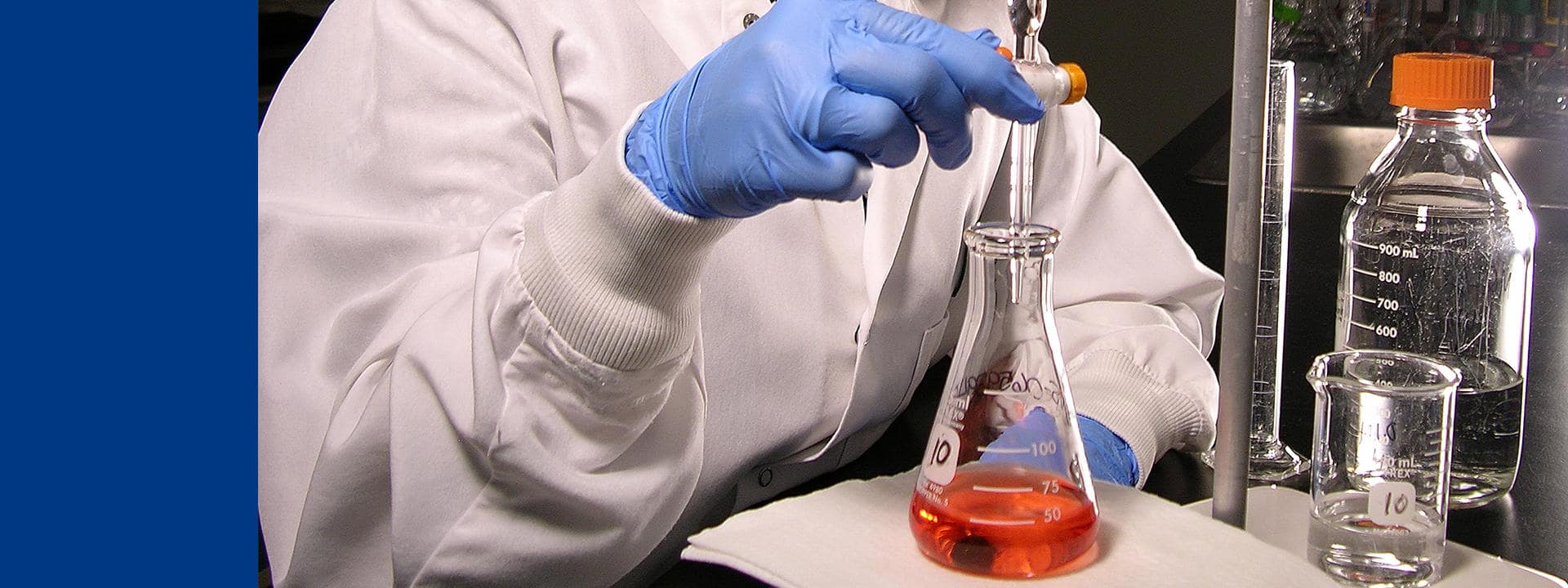 Technicien de laboratoire Eurofins BioPharma Product Testing effectuant une manipulation de précision à l’aide d’une pipette pour transférer un liquide dans un Erlenmeyer contenant une solution colorée. L’image illustre les procédures rigoureuses de contrôle qualité et d’analyse physico-chimique des matières premières utilisées dans la fabrication de produits pharmaceutiques, dans un environnement conforme aux normes de sécurité et de traçabilité.