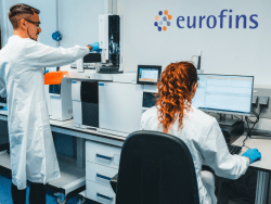 Laboratoire Eurofins BioPharma Product Testing : deux techniciens de laboratoire réalisent un test d’aptitude du système dans un environnement de contrôle qualité conforme aux normes GMP. L’un manipule un équipement analytique, l’autre travaille sur un poste informatique. Le logo Eurofins visible sur le mur renforce l’identité du site, spécialisé dans les analyses pharmaceutiques, la validation des méthodes, et la qualification des systèmes, y compris les points de prélèvement et les boucles de distribution