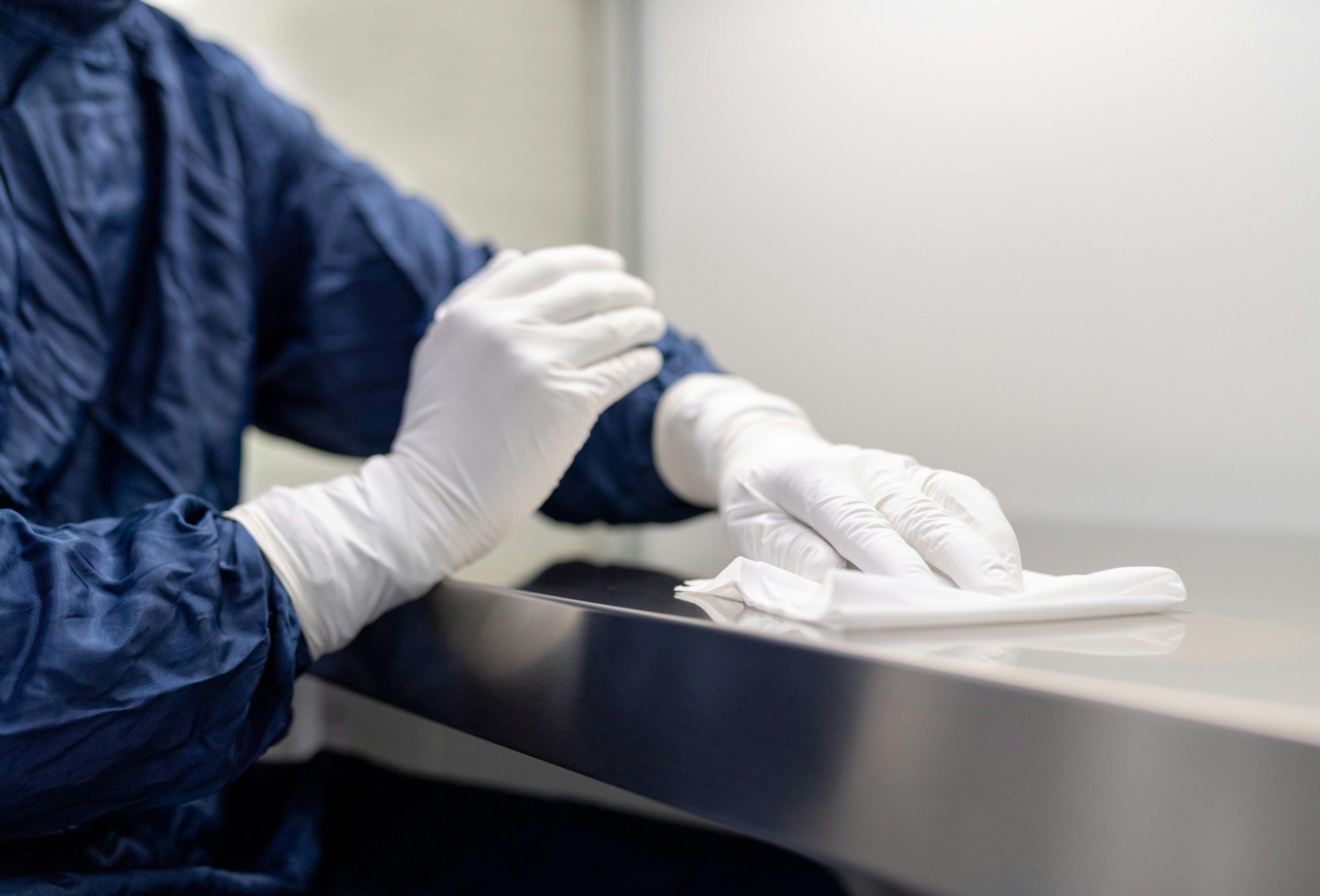 Technicien procédant à la désinfection d'une surface en acier inoxydable dans un environnement contrôlé, illustrant les standards élevés de propreté et de sécurité appliqués par Eurofins BioPharma Product Testing dans le cadre de ses services de contrôle qualité pharmaceutique.