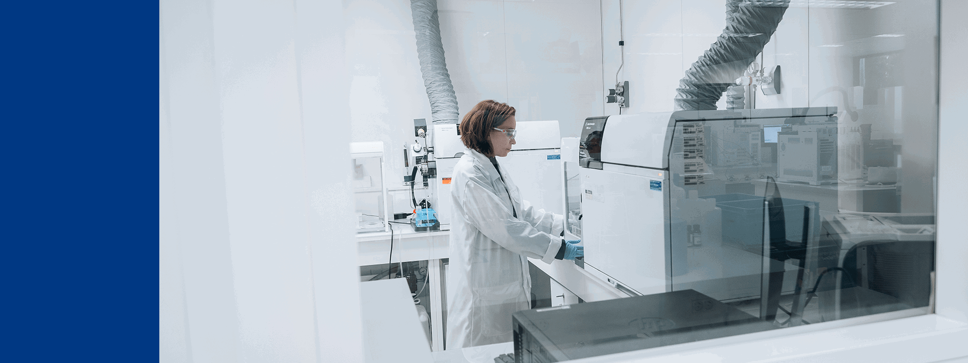 Laboratoire Eurofins BioPharma Product Testing équipé pour des analyses de haute précision. Une personne en blouse blanche et gants de protection manipule un instrument analytique sophistiqué dans une salle propre, conçue pour garantir la conformité aux normes GMP. L’environnement comprend des systèmes de ventilation et d’extraction, des équipements de mesure et des surfaces stériles, illustrant les standards élevés de qualité et de sécurité appliqués aux tests biopharmaceutiques.