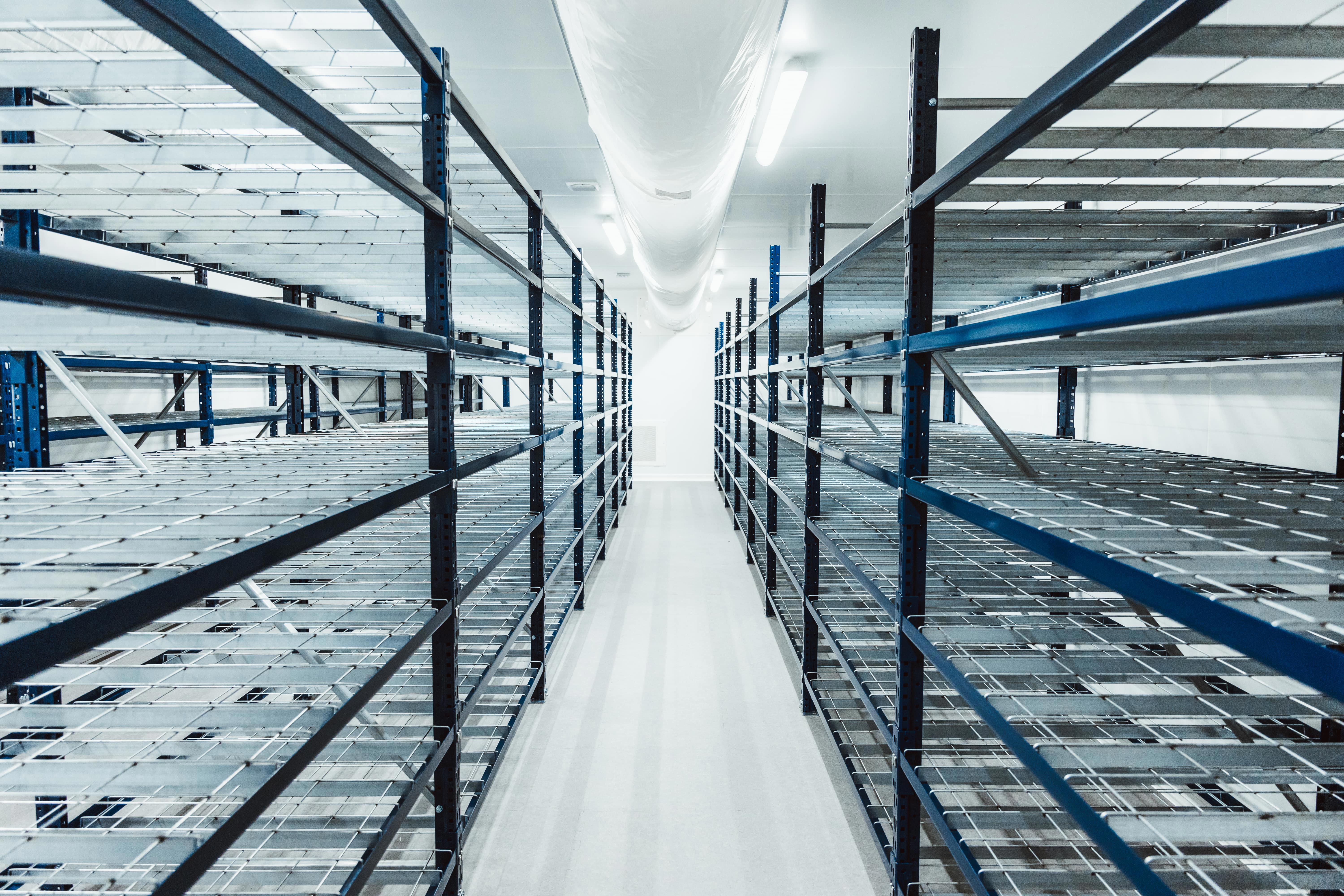 Vue d’un espace de stockage industriel vide, équipé de rayonnages métalliques robustes disposés en rangées parallèles. L’environnement est propre, bien éclairé et conçu pour accueillir des équipements ou des échantillons dans le cadre des activités de tests comparatifs ou de gestion logistique chez Eurofins BioPharma Product Testing.