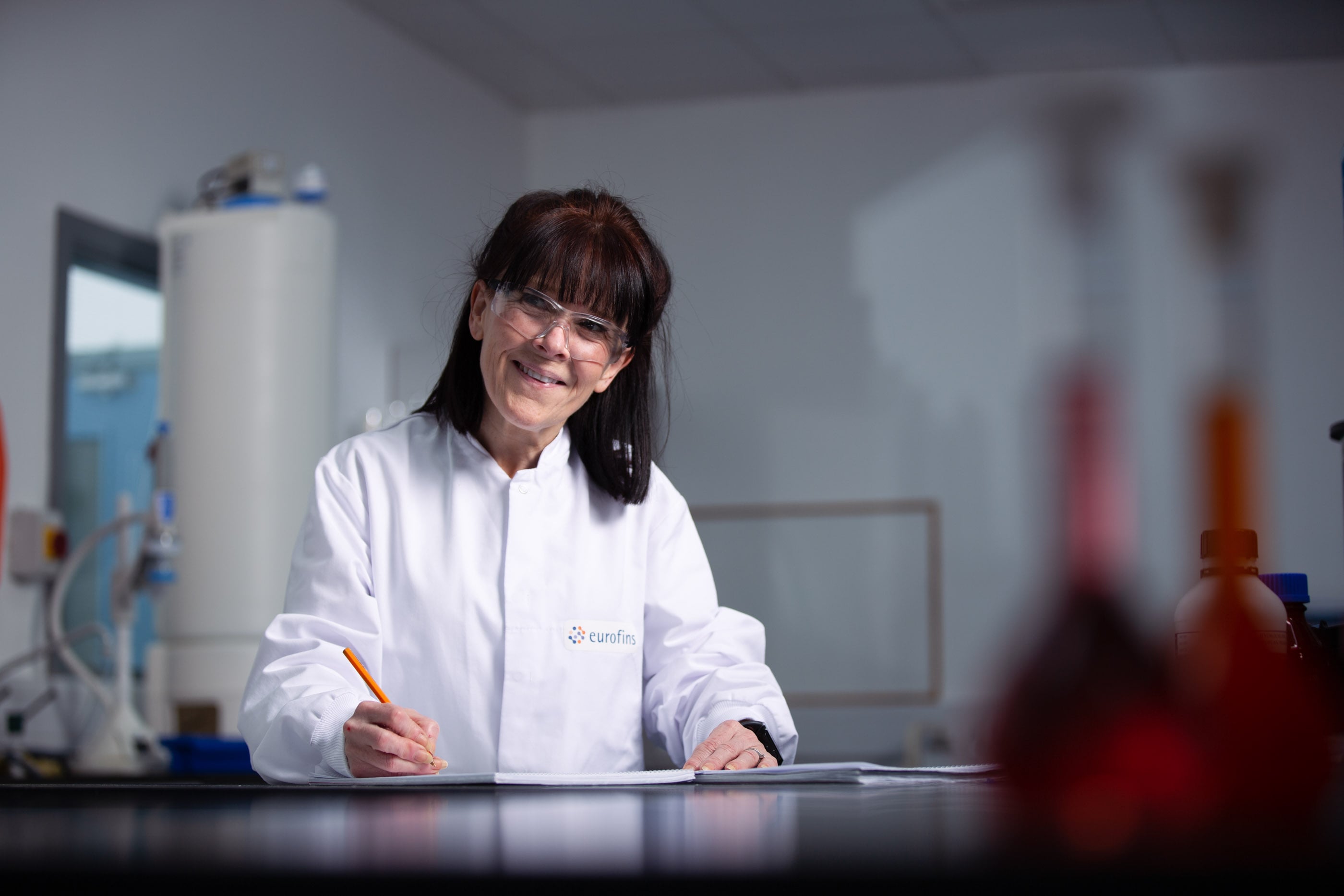 Technicien en blouse blanche Eurofins BioPharma Product Testing réalisant un prélèvement et une traçabilité documentaire dans un laboratoire pharmaceutique. L’image illustre les contrôles qualité effectués sur les systèmes de gaz comprimé et d’eau purifiée, essentiels pour la qualification des utilités critiques, la conformité aux normes GMP et la sécurité des procédés biopharmaceutiques.