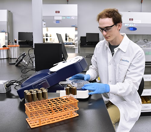 Test d’endotoxines bactériennes par méthode recombinant Factor C (rFC) dans un laboratoire Eurofins BioPharma Product Testing : un opérateur en blouse blanche et lunettes de protection manipule un analyseur automatisé. Des tubes à essai avec bouchons dorés sont disposés dans un support orange sur la paillasse. Cette procédure fait partie du contrôle qualité microbiologique des produits pharmaceutiques injectables, conforme aux exigences des pharmacopées internationales.