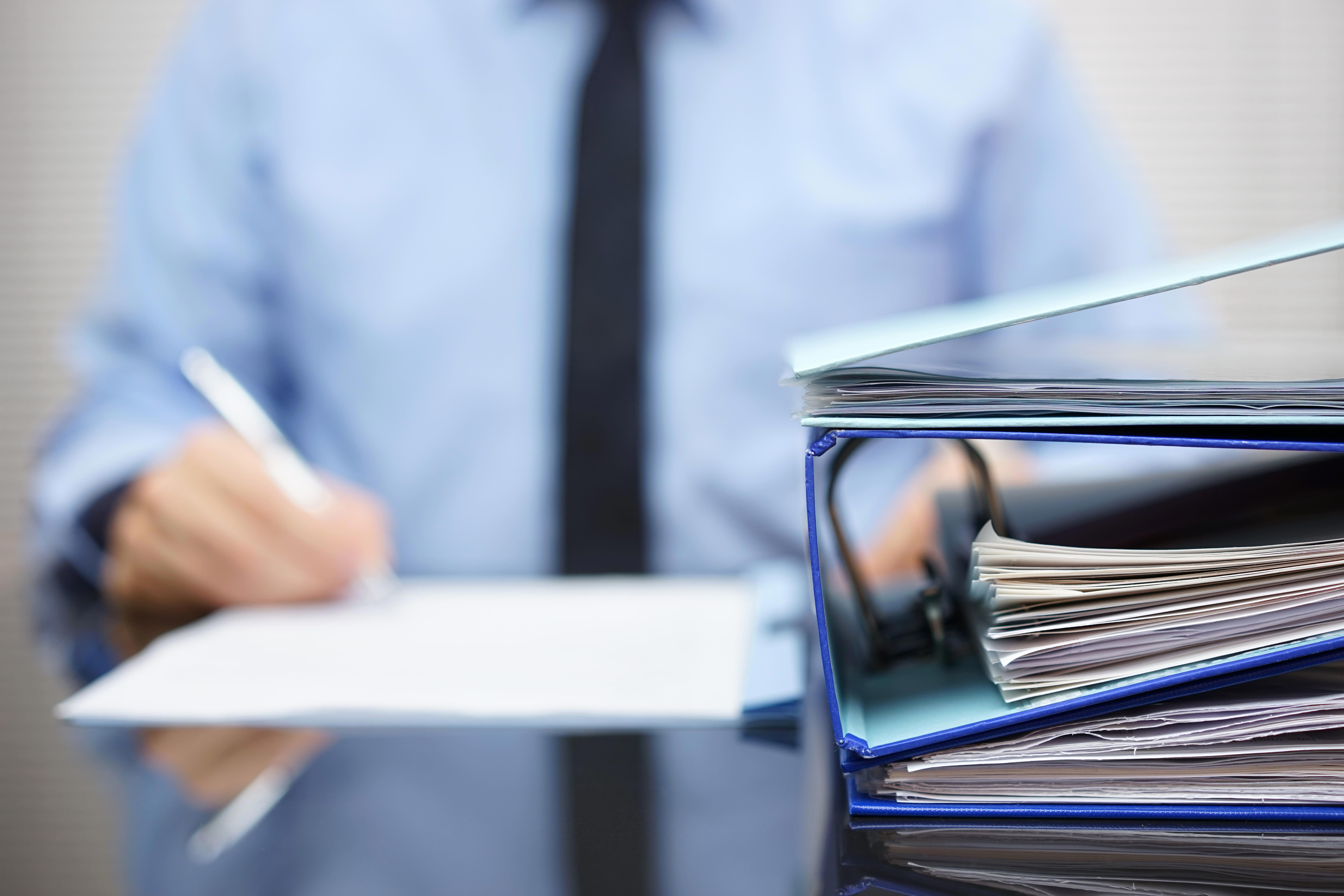 binders-with-papers-are-waiting-to-be-processed-with-businessman-back-in-blur-xl_9000x6000px-1