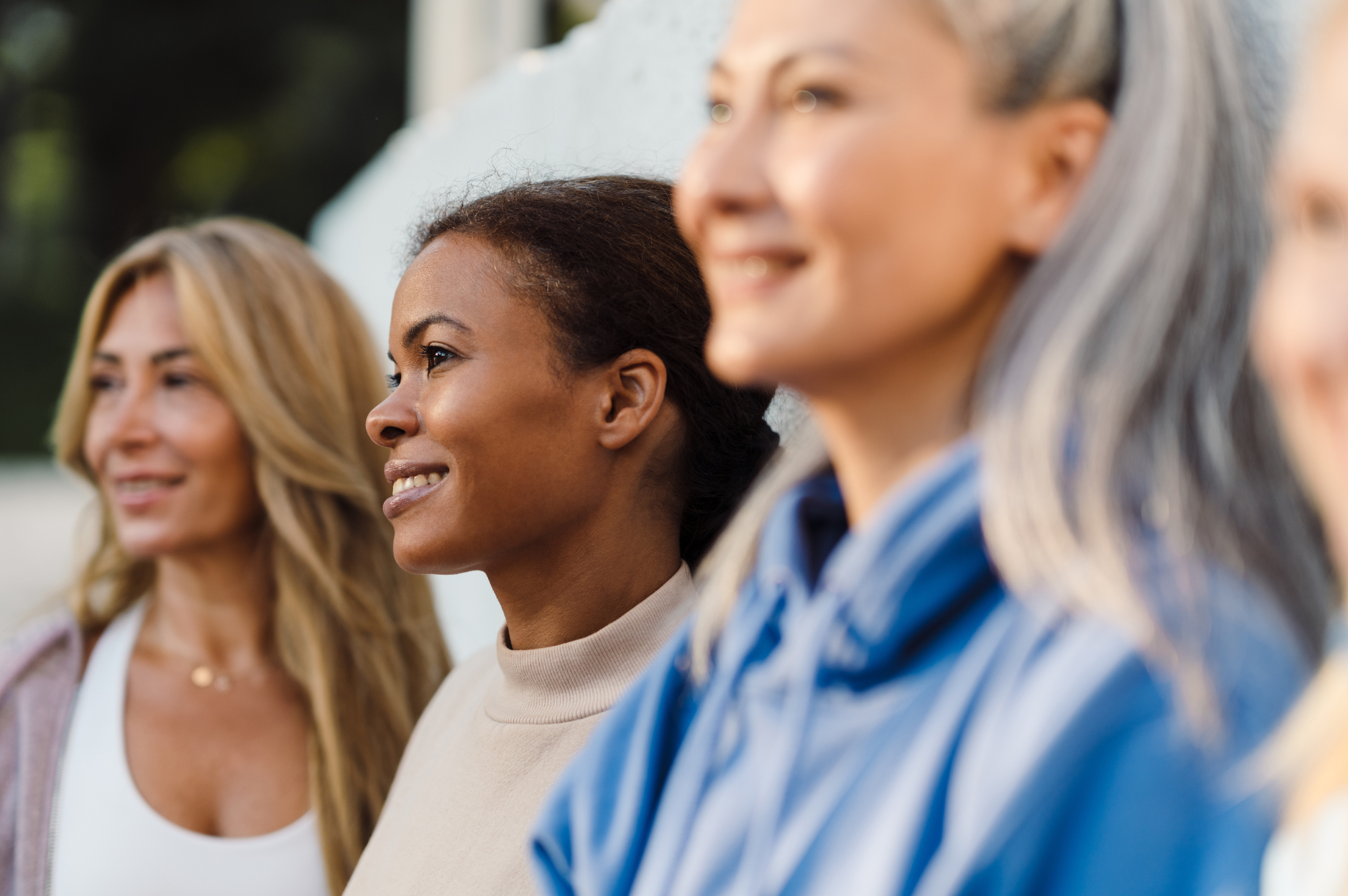 multiracial-women-talking-and-laughing-after-yoga-practice-while-leaning-on-wall-outdoors