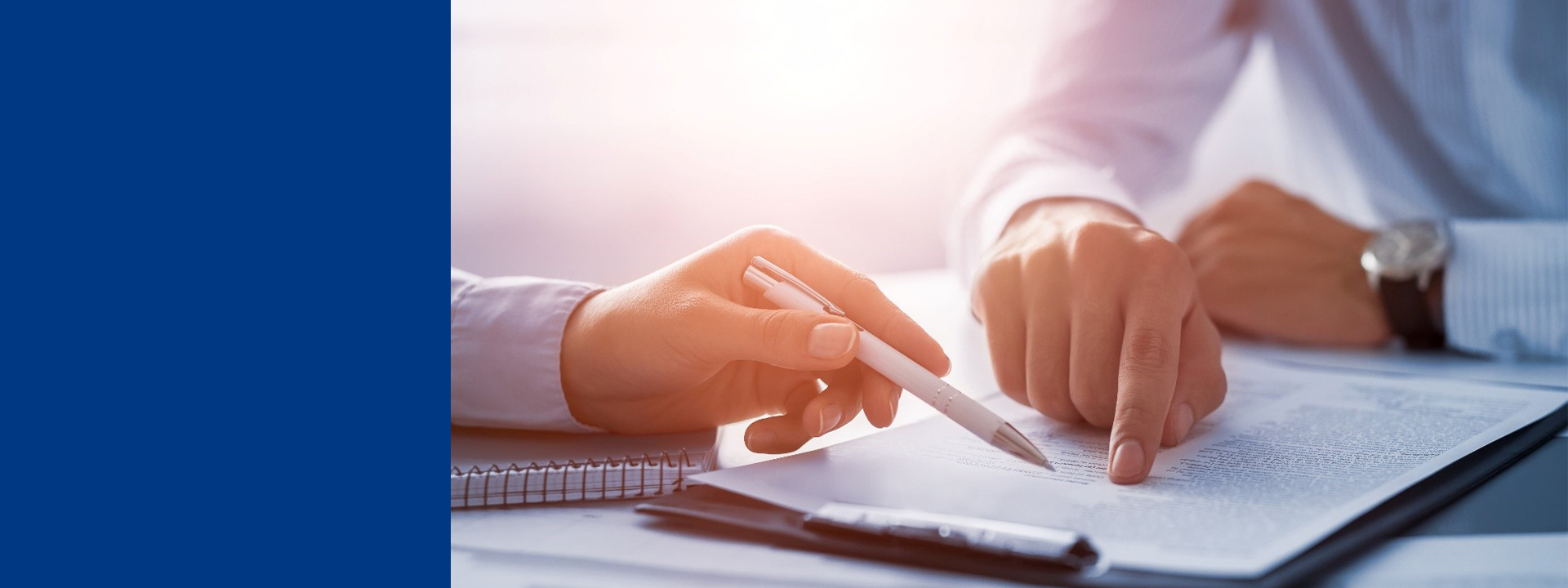 Close-up of two individuals’ hands pointing at and reviewing a printed document on a desk, with a notebook visible nearby, representing collaborative document review or analysis.