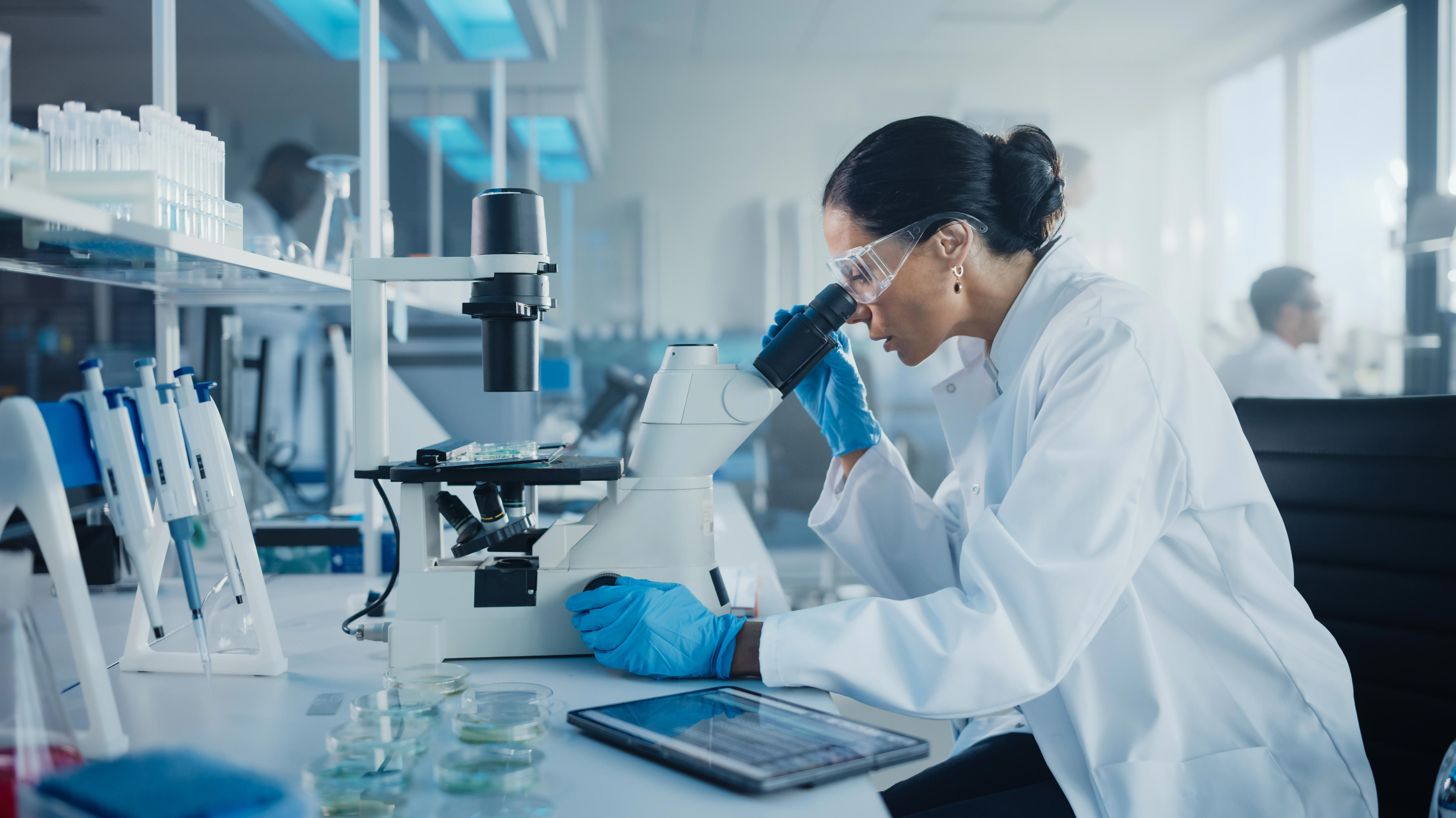 medical-development-laboratory-caucasian-female-scientist-looking-under-microscope-analyzes-petri-dish-sample-specialists-working-on-medicine-biotechnology-research-in-advanced-pharma