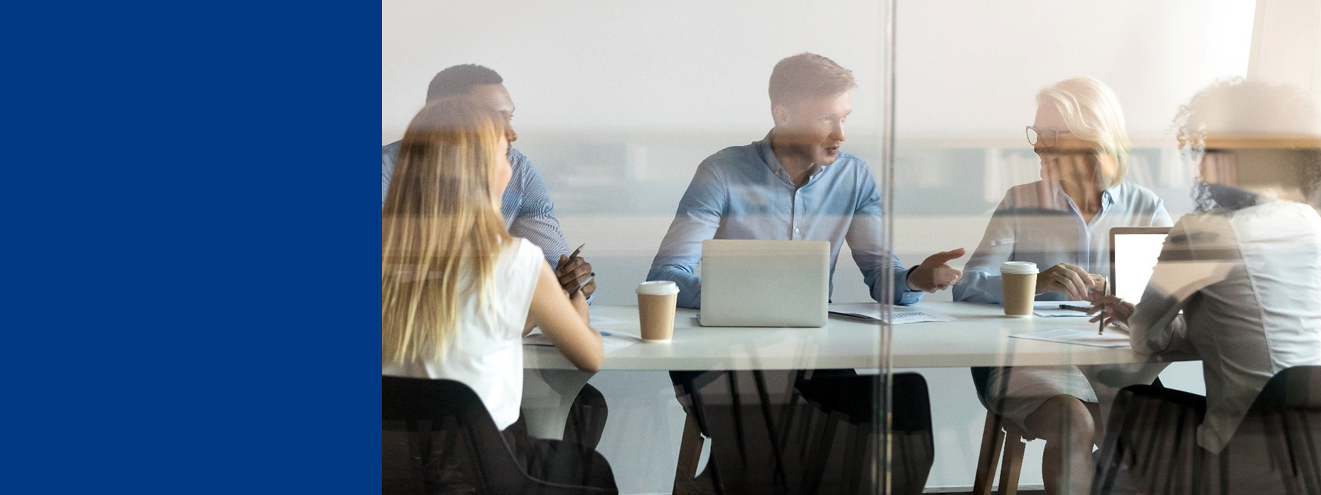 Blurred image of a group of professionals seated around a conference table in a modern office, collaborating with laptops and documents, suggesting a team meeting or discussion.