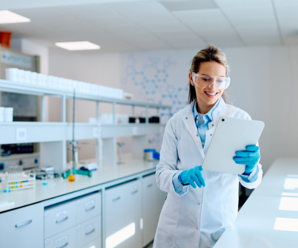 female-scientist-wearing-safety-glasses-and-lab-coat-smiling-while-analyzing-data-on-a-tablet-in-a-modern-research-laboratory